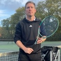 Photo of Alex Hicks tennis coach in a black tracksuit holding a green racket